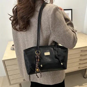 Glossy black tote bag with gold metal plate and woven charm for daily commuting style