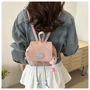 Mini pink backpack with plush charm detail shown on a model in a casual home setting