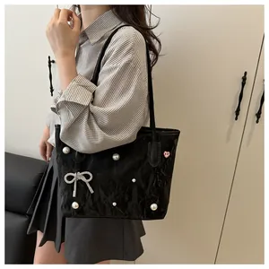 Detail of black tote bag featuring white pearls and a sparkling silver bow pendant charm