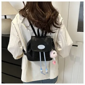 Close-up of black mini backpack featuring a logo patch and pink plush charm