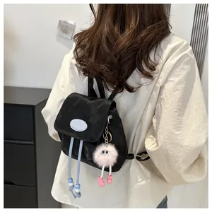 Close-up of a black mini backpack with blue drawstrings and a pink plush monster charm