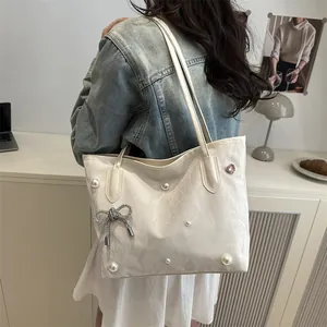 Elegant off-white PU tote bag with pearl embellishments and bow charm on a model
