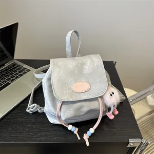 Mini metallic light gray backpack with pink logo and plush monster charm on desk