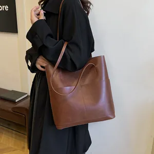 Brown large capacity tote bag in oil wax leather with external pockets shown on shoulder