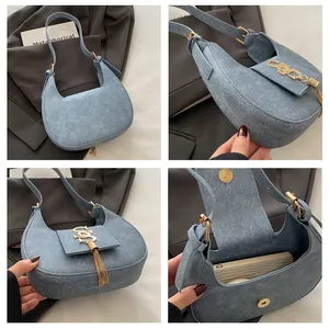 Détail du sac demi-lune en daim bleu clair avec boucle S dorée et finition à franges