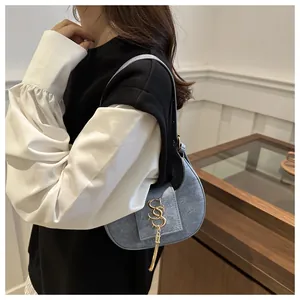 Détail du sac croissant en denim bleu avec logo SS doré et franges en chaîne