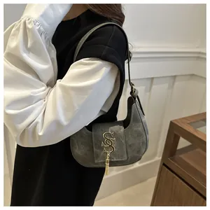 Détail du sac demi-lune en daim gris avec logo SS en métal doré et pompon élégant