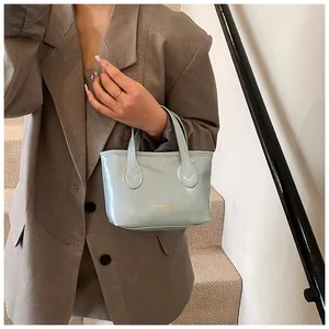 Detail of light blue glossy handbag with gold lettering held by a model in a brown blazer