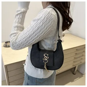 Détail du sac hobo croissant noir avec logo doré et pompon tenu par un mannequin