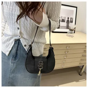 Détail du sac croissant noir avec logo en métal doré et pompon sur matière en suédine