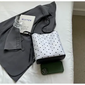 Détail du sac seau blanc à pois avec fond en cuir noir posé sur un lit blanc élégant
