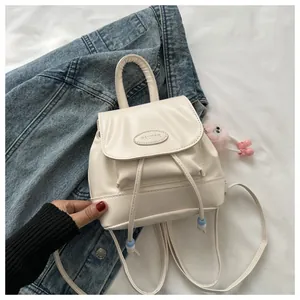 Detailed macro view of a cream mini backpack featuring a plush pink ball charm
