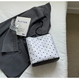 Détail du sac seau blanc à pois avec dentelle sur un fond de blazer gris foncé