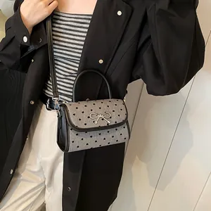 Chic mini crossbody bag with heart pattern and silver bow, styled on a black trench coat