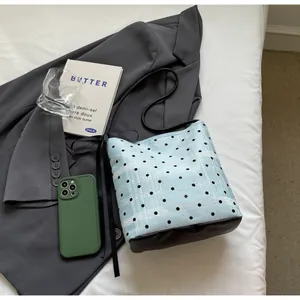Détail du sac seau à pois bleu clair avec base en cuir noir sur un blazer gris