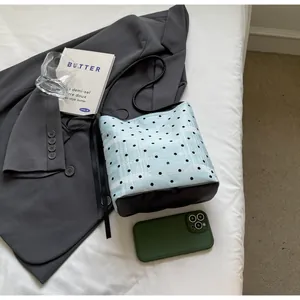 Vue détaillée du sac seau en tweed bleu clair à pois et cuir noir sur un tissu blanc doux