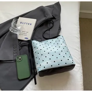 Détail d'un sac seau bleu à pois avec rayures en dentelle et base en cuir sur lin blanc