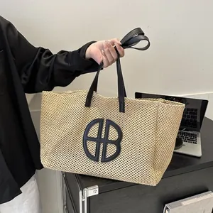 Grand cabas en paille tressée beige avec anses en cuir noir et logo central distinctif