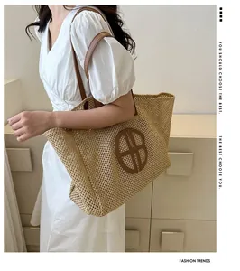 Détail d'un grand sac cabas en paille avec bandoulières en cuir marron et écusson logo