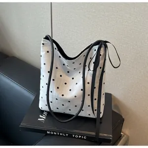 Détail d'un sac seau en toile blanche à pois noirs avec fine bandoulière en cuir