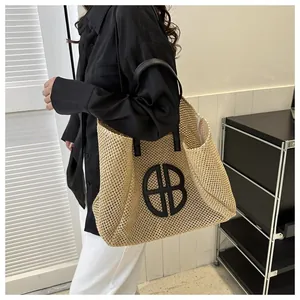 Photo lifestyle d'un grand sac cabas en paille avec lanières en cuir noir et logo