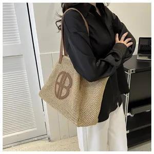 Vue détaillée d'un sac cabas en paille tressée avec anses en cuir brun et logo BB