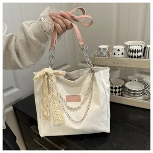 Detail of white tote bag with lace bow, pearl charm, and pink leather handles