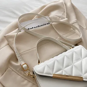 Detail of white quilted handbag featuring a gold bar fastener and adjustable thin strap