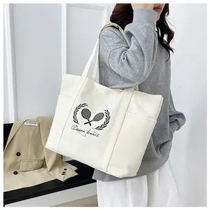 Detail showing high-capacity canvas tote bag with side pocket and Queen tennis print