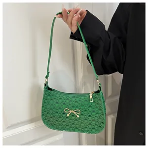 Close-up of green handbag featuring textured fabric and gold bow accent held by a model