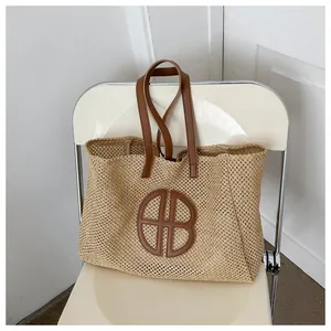 Détail d'un sac cabas en paille tissée avec anses en cuir marron et logo HB chic