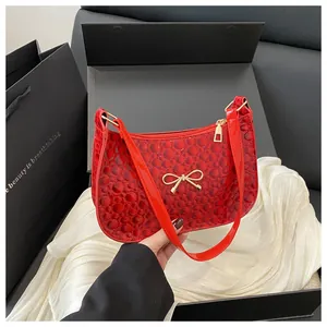 Detail of red patent leather shoulder bag with bubble texture and gold bow ornament