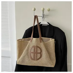 Détail du sac cabas en paille beige avec anses en cuir marron et logo rond