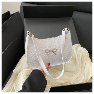 Close-up of white embossed half-moon bag with golden bow hardware on black gift box