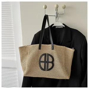 Détail d'un cabas en paille avec logo en cuir noir et bandoulières sur un blazer