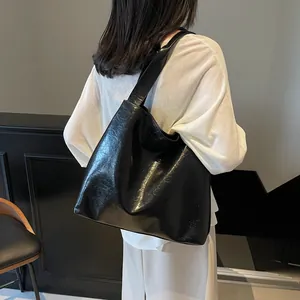Glossy black leather tote bag for women with wide shoulder strap in a minimalist style