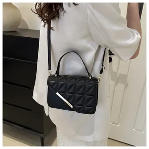 Detail of black quilted shoulder bag with gold metal trim worn by model in minimalist setting