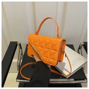 Detailed shot of orange quilted handbag with golden metal bar and geometric stitching