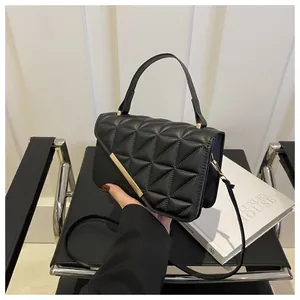 Detail of black quilted leather handbag with gold metal bar and top handle on a chair