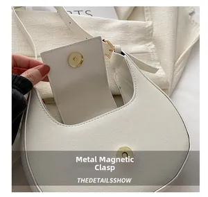 Close-up of golden magnetic buckle on white cross-grain leather crescent shoulder bag