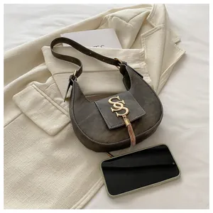 Detail of vintage suede hobo bag with golden logo and metallic tassel on beige blazer