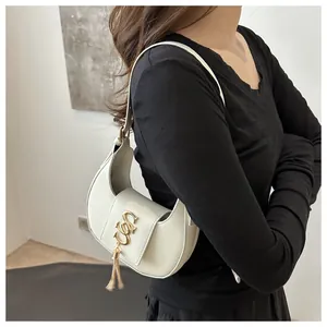 Close-up of creamy white crescent shoulder bag with golden hardware logo and tassel