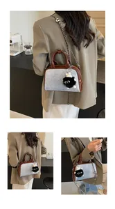Detalle de bolso bandolera de mezclilla gris con asas de cuero marrón y amuleto monstruo