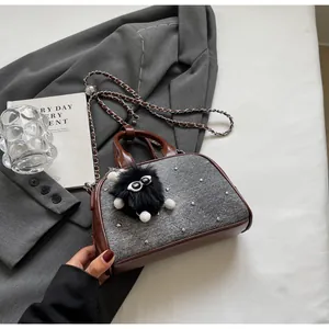Detalle del bolso denim con ribete de cuero, remaches metálicos y colgante de pompón negro