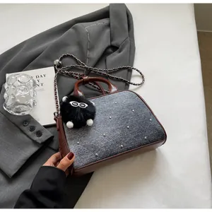 Detalle del bolso bandolera vaquero con acolchado en V, tachuelas plateadas y amuleto peluche