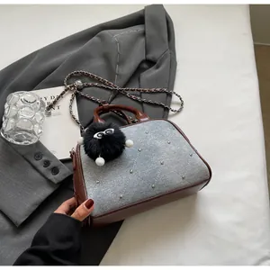 Detalle de bolso bandolera de mezclilla y cuero marrón con tachuelas sobre chaqueta gris