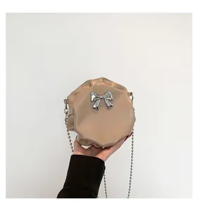 Détail du sac à bandoulière rond plissé beige avec nœud argenté et bandoulière chaîne