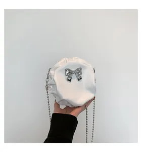 Détail d'un sac rond plissé blanc avec nœud argenté et bandoulière en chaîne à billes