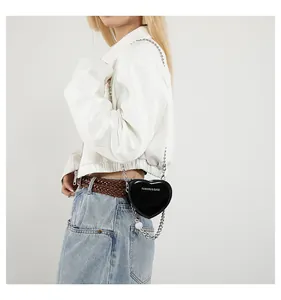 Detail of a black heart-shaped mini crossbody bag with silver chain strap worn by model