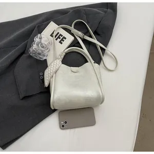 Détail du sac seau blanc crème avec foulard décoratif sur l'anse et texture de cuir fin